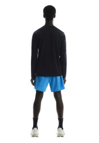 Langærmet sort atletisk skjorte parret med blå shorts, der har en afslappet pasform og letvægtsstof, vist fra ryggen.