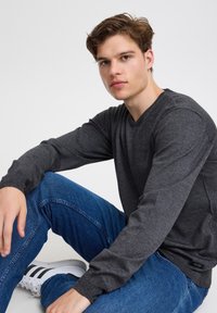 Donkergrijze gebreide trui met een V-hals, gecombineerd met blauwe jeans en witte sneakers met zwarte strepen.