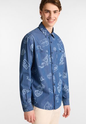 Blauwe denimshirt met een subtiel patroon van verschillende emblemen en logo's. Het heeft een knoopsluiting aan de voorkant en twee borstzakken. Langsleeves ontwerp.