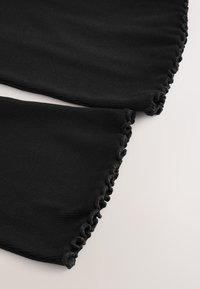 Primer plano de tela negra acanalada con bordes fruncidos sobre un fondo claro, mostrando textura y detalles de costura.