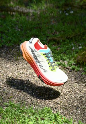 Hardloopschoen met een witte bovenkant, multicolore accenten waaronder geel en blauw, en een dikke oranje-rode zool. Bevat gestructureerde veters.