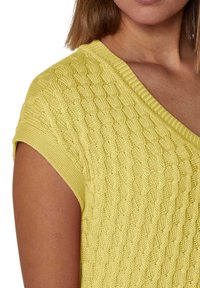 Gelber Strickpullover mit V-Ausschnitt und kurzen Ärmeln, der ein strukturiertes Zopfmuster aufweist. Der Stoff wirkt weich mit einem leichten Glanz.