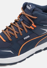 Baskets montantes bleues avec des accents orange et des superpositions texturées. Elles présentent des lacets épais, un collier rembourré et une semelle en caoutchouc robuste.