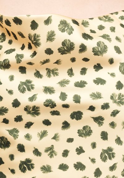 Κρεμ υφασμάτινο με διάσπαρτα σκούρα πράσινα σχέδια φύλλων, ελαφρώς τσαλακωμένο για να δείξει υφή και ροή.