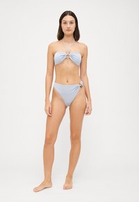 Világoskék bikini, amely bandeau fazonú felsőrésszel rendelkezik, csavart dizájnnal és kör alakú kiegészítőkkel, alacsony derekú alsókkal párosítva, amelyeket oldalsó csomó díszít.