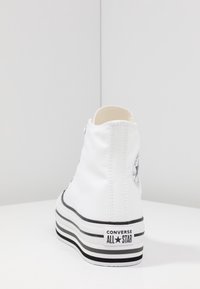 Baskets montantes en toile blanche avec accents noirs, dotées d'une semelle en caoutchouc, d'une pointe ronde et d'un logo en patch sur le côté extérieur.