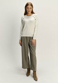 Kremowy sweter z prążkowanej tkaniny, ozdobiony sztucznymi guzikami na ramionach, zestawiony z wysokim stanem, szerokimi spodniami w kratę w ziemistych odcieniach oraz botkami na obcasie.