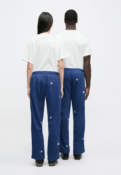 Blue sweatpants with rabbit embroidery, paired with plain white T-shirts. The fabric appears soft with an elastic waistband.