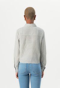 Striped gray corduroy shirt with long sleeves and a collared neckline, featured on a person wearing blue jeans, viewed from the back.