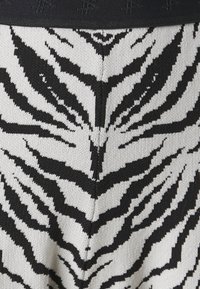 Pletene legginge z vzorcem črno-bele zebra črte, s črnim pasom in teksturirano tkanino.