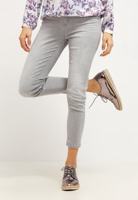 Jeans skinny de color gris claro con una textura suave, combinados con zapatos metálicos plateados con cordones que tienen una suela beige en contraste.