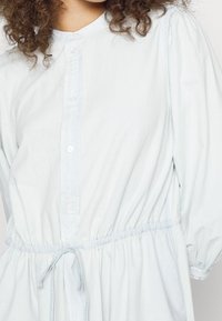 Abito blu chiaro, con bottoni, colletto rotondo, vita elastica e maniche a sbuffo. Tessuto morbido con una vestibilità comoda e dettagli con fiocco.