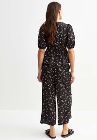 Černý květinový top s peplum střihem a nabíranými rukávy, v kombinaci s černými kalhotami širokého střihu. Materiál má malé růžové a žluté květinové vzory.