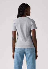 Grå t-shirt med korte ærmer og rund halsudskæring, tætsiddende pasform og blød overflade, parret med lyseblå højtaljede denimjeans.