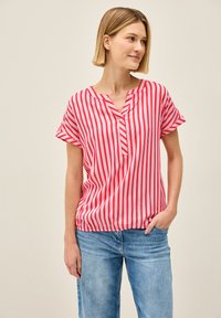 Rød- og hvidstribet kortærmet bluse med v-hals, afslappet pasform og elastisk kant. Sammen med lyseblå denimjeans.