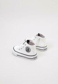Zapatillas altas blancas de material sintético, con un parche redondo con logo, detalles en negro y una suela texturizada. Detalle de cremallera en el costado.