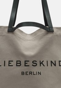 Torebka płócienna w jasnoszarym kolorze z czarnymi skórzanymi uchwytami. Na torbie widnieje napis "LIEBESKIND BERLIN" drukowany grubą czcionką w kolorze czarnym. Teksturowana powierzchnia materiału.