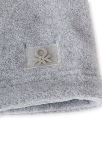 Tessuto felpato grigio con una toppa trasparente che presenta un logo minimalista. Texture morbida con una finitura liscia e dettagli di bordo piegato.