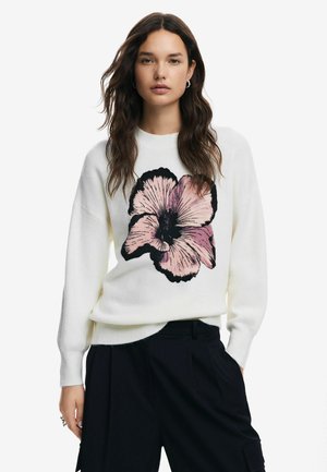 White sweater with a large black and pink flower print on the front. Features a crew neckline and ribbed cuffs. Paired with dark pants.