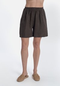 Shorts in lino marrone con vita elastica, vestibilità rilassata, che arrivano sopra il ginocchio. Abbinati a scarpe slip-on in tessuto beige.
