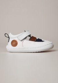 Zapato de cuero blanco con correas marrones y marinas, parche de logo circular, lengüeta elástica en el talón y suela de goma texturizada. Diseño de punta cerrada.