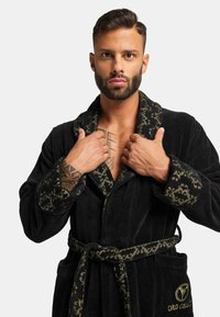 Black velour robe with a patterned green collar and cuffs. Features a tie belt and pockets, with embroidered logo on the chest.