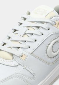 Šviesiai mėlynas odinis sportbačių su baltomis raišteliais, lygiu paviršiumi, siūtais akcentais ir apvalios formos logotipo detale šone.