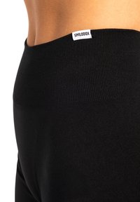 Leggings noirs avec une taille côtelée comportant une étiquette blanche cousue portant la mention "SMILODOX". Le tissu semble lisse et extensible.