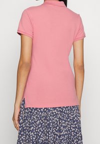 Short-sleeve polo shirt in soft pink cotton, featuring a classic collar and side slits, paired with a floral-patterned skirt.