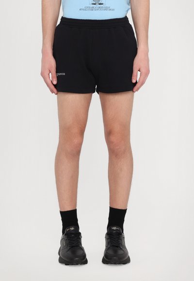 Schwarze Sportshorts mit elastischem Bund, ausgestattet mit einem kleinen Logodetail. Kombiniert mit schwarzen Socken und leichten schwarzen Turnschuhen.