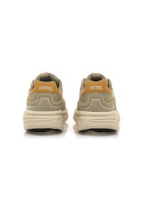 Zapatillas beige con parte superior de tejido texturizado, que presentan una pestaña en el talón y logotipo amarillos, forma redondeada y suela blanca gruesa.
