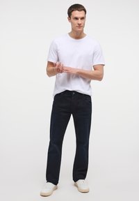 T-shirt bianca a girocollo abbinata a jeans blu scuro. I jeans presentano tasche frontali, chiusura con bottone e leggere scoloriture. Completa il look con sneakers bianche.