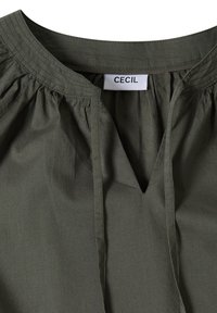 Col de chemise vert foncé avec un décolleté en V et un tissu froncé près du cou, avec une étiquette de marque blanche indiquant "CECIL".