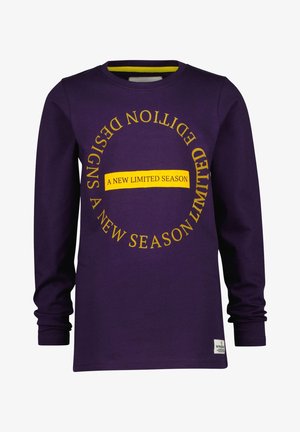Chemise à manches longues violet foncé avec un texte jaune en cercle indiquant "UN NOUVEAU DESIGN SAISON LIMITÉE" et un rectangle jaune avec "UNE NOUVELLE SAISON LIMITÉE."