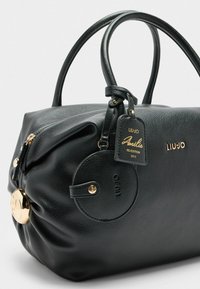 Zwarte leren handtas met een textuur, in een ronde vorm, gouden hardware accenten, een cirkelvormig label en de merknaam "LIU-JO" erin geperst.