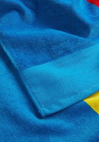 Tessuto blu texturizzato con un bordo liscio e piatto, caratterizzato da accenti colorati di giallo e rosso. Il materiale sembra morbido e leggermente soffice.