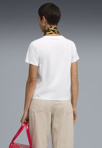 Witte, kortlang t-shirt met een ontspannen pasvorm, in combinatie met beige linnen broeken. Een sjaal met luipaardprint is om de nek geknoopt.