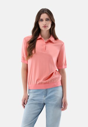 Polo a maniche corte in satin corallo con una vestibilità slim, chiusura a bottoni e orlo a costine. Indossato con jeans rilassati azzurri.