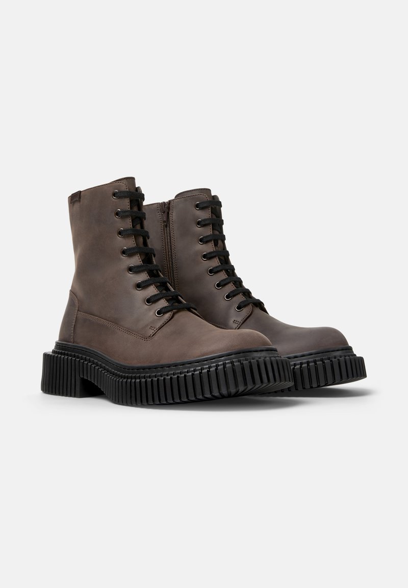 Bottes en cuir brun à la cheville avec des lacets noirs, bouts ronds et semelle en caoutchouc texturée épaisse. Dotées d'une fermeture éclair sur le côté pour un enfilage facile.