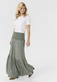 Maksi krilo v zeleni barvi s vijoličnim cvetličnim vzorcem in smukastim pasom; v kombinaciji z belim rebrastim zgornjim delom z valovitim robom. Rjave škornje s peto.