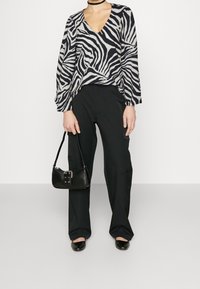 Blouse imprimé zèbre en gris et noir, manches longues, col en V, associée à un pantalon cargo noir et un petit sac à main noir. Chaussures plates noires.