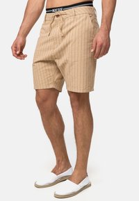 Beige stribede shorts i et letvægtsstof med snor og knaplukning. Sammen med hvide slip-on sko med en tekstureret sål.