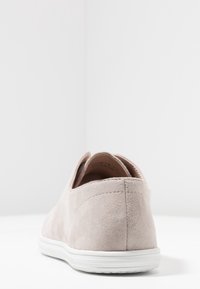 Zapatilla de ante en color beige claro con un acabado texturizado y suela de goma blanca. Presenta un diseño de perfil bajo y detalles de costura sutiles.