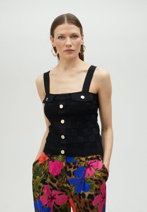 Schwarzes geripptes Tanktop mit quadratischem Muster, breiten Trägern und goldenen Knöpfen. Kombiniert mit blumigen, tiermusterierten Hosen.