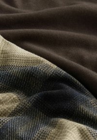 Tekstiler i forskellige farver: et mørkebrunt glat stof lagdelt med et mønstret beige og marineblåt stof med striber og tern.