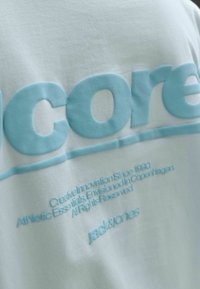 Tissu blanc avec texte en relief bleu clair "core" et texte plus petit sur l'innovation créative et la marque Jack & Jones, en gros plan.