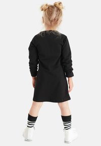 Czarna długa sukienka z luźnym krojem, z zaokrąglonym dołem. Połączona z czarno-białymi skarpetami w paski i białymi trampkami za kostkę.