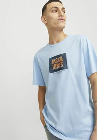 Svijetloplava majica kratkih rukava s pravokutnim crnim i narančastim grafičkim uzorkom na kojem je u središtu ispisano "JACK & JONES".