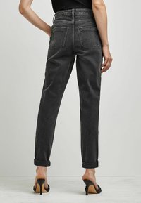 Höga svarta denimjeans med avslappnad passform, upprullade fållar och två bakfickor synliga från baksidan.