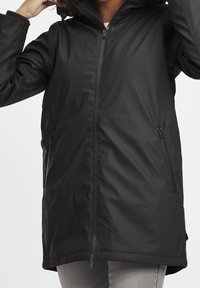 Czarna wodoodporna kurtka z zamkiem z przodu, regulowanym kapturem i dwiema bocznymi kieszeniami, o gładkim, matowym wykończeniu i średniej długości kroju.